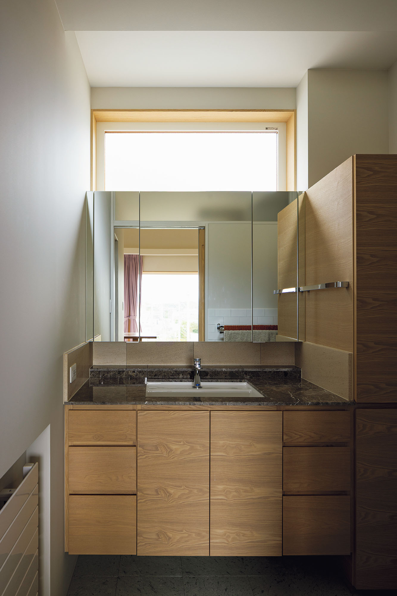 造作洗面台は、タオル類などをしまう収納も充実させた。床と洗面天板は天然石仕上げ